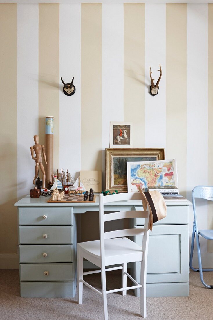Desk and chair below hunting trophies hung on striped wallpaper