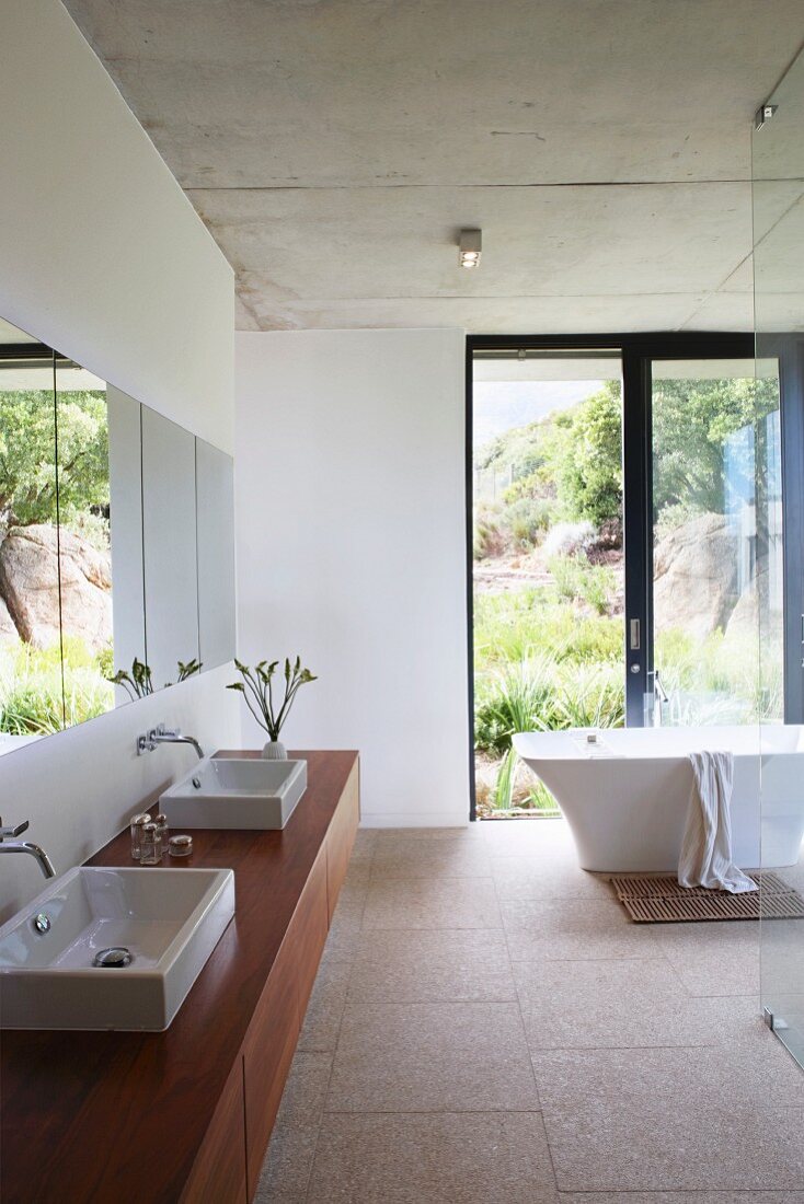 Waschtisch mit zwei Aufsaztbecken auf Holzunterbau, im Hintergrund freistehende Badewanne vor Terrassentür in minimalistischem Bad