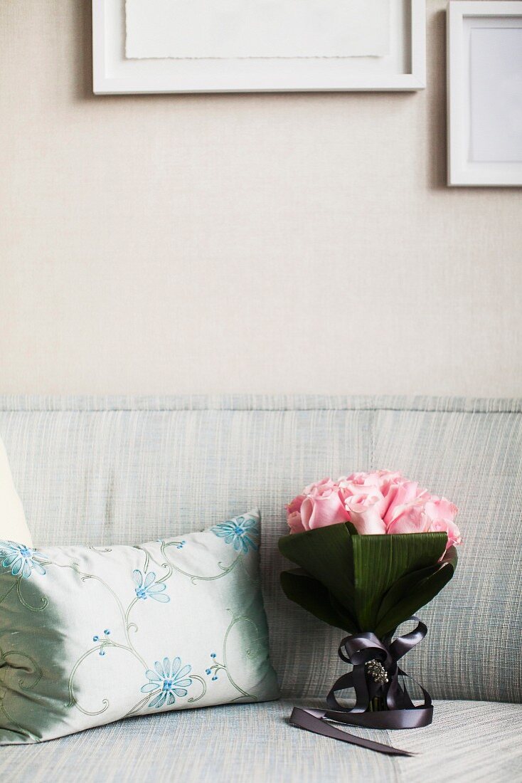 Rosenstrauss auf Sofa neben silberfarbenem Zierkissen