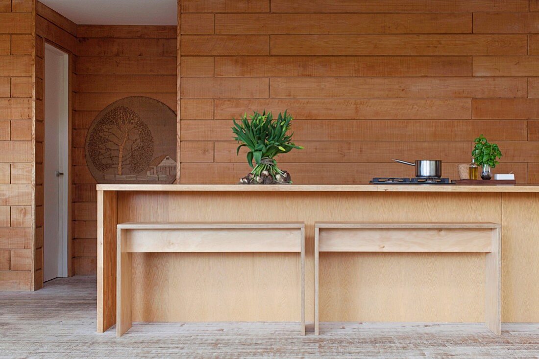 Minimalist wooden kitchen counter and benches in front of wood-clad wall