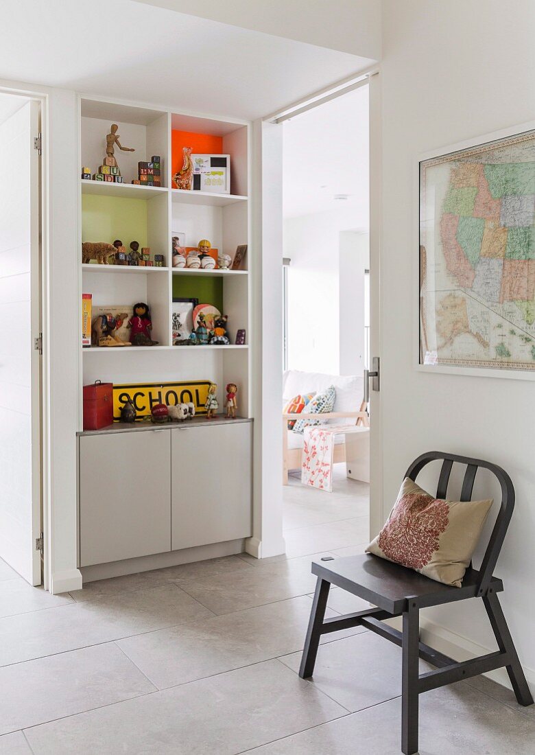 Grey-painted chair against wall and shelves and cupboards built into niche in foyer