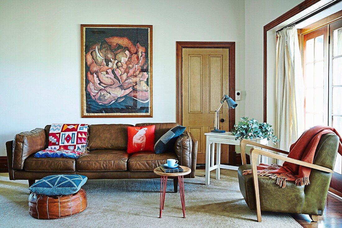 Cushion on pouffe in front of traditional brown leather sofa and fifties-style armchair in eclectic living room