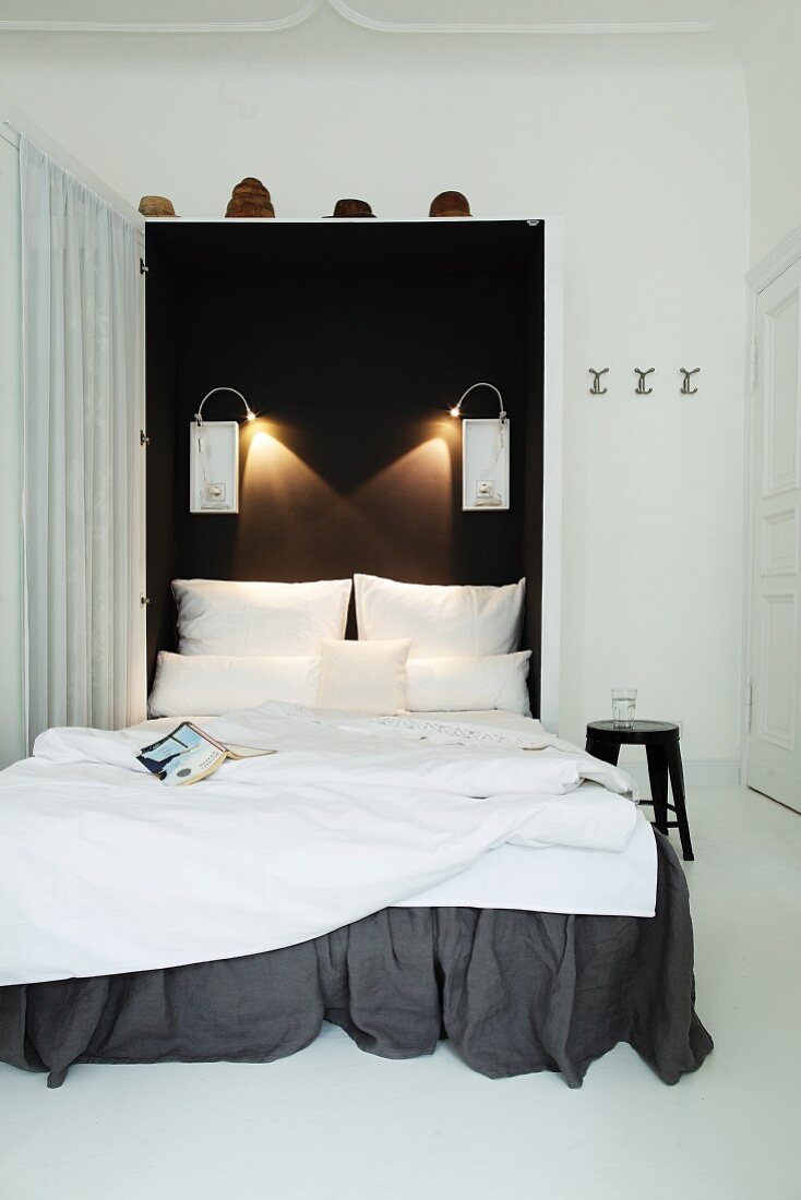 Wandbett mit dunkelgrauer Husse, weiße Bettwäsche vor schwarzer Wand mit Beleuchtung