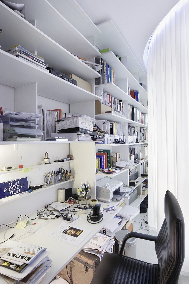Moderner Arbeitsplatz hinter Vorhang - weiße Regale an Wand mit integrierter Schreibtischplatte, schwarzer Bürostuhl