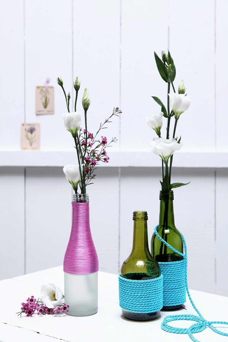 Verschiedene Flaschen mit farbigen Kordeln umwickelt als Blumenvasen