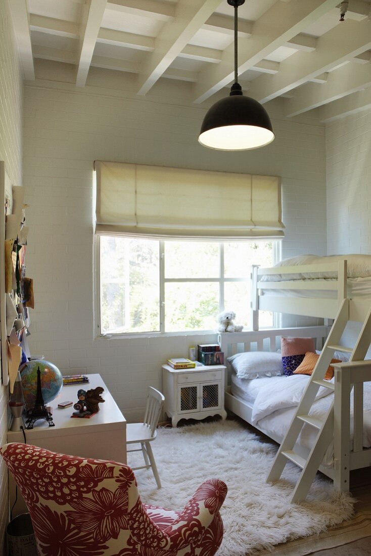 White flokati rug next to bunk beds in children's bedroom with white wooden ceiling and patterned armchair in foreground
