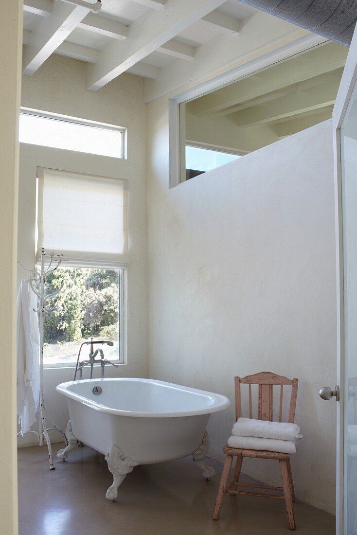 Blick durch offene Tür auf freistehende Vintage Badewanne vor Fenster, seitlich Oberlicht in Zimmerwand