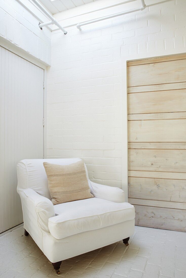 Traditioneller Sessel mit weißem Bezug in Zimmerecke, geweisselte Ziegelwände