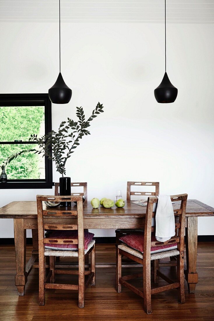 Designer pendant lamp with black lampshade (Tom Dixon) above rustic wooden chairs and table