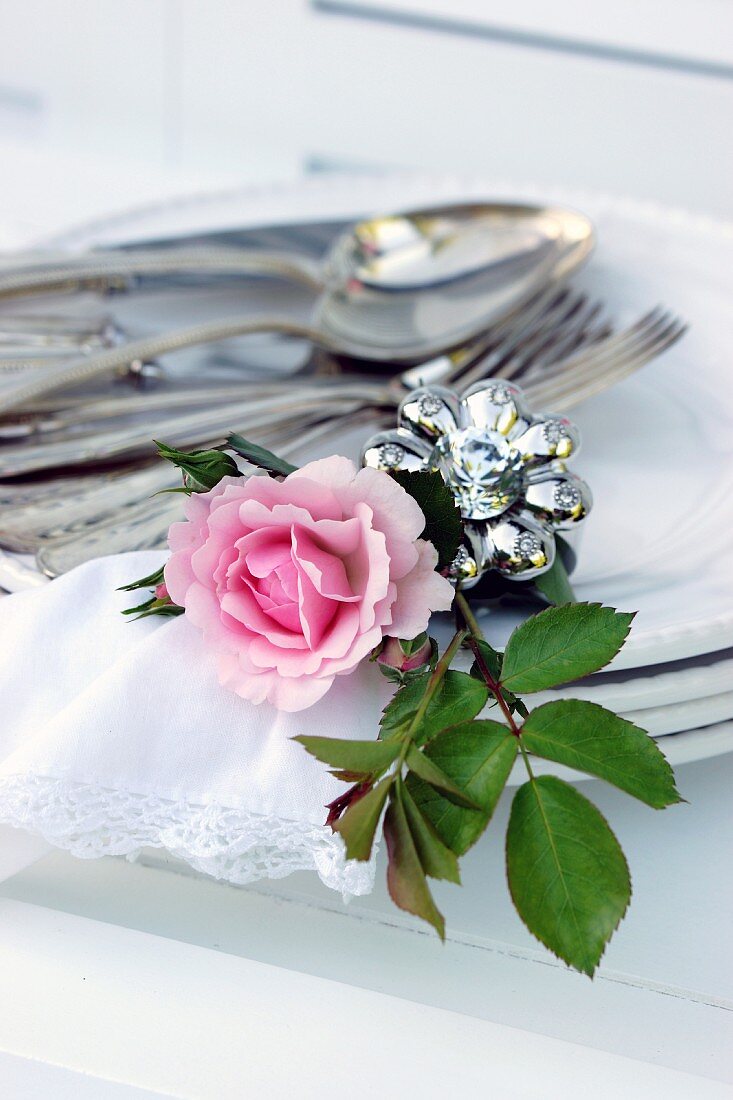 Silver cutlery, napkin ring, rose & linen napkin on stacked plates