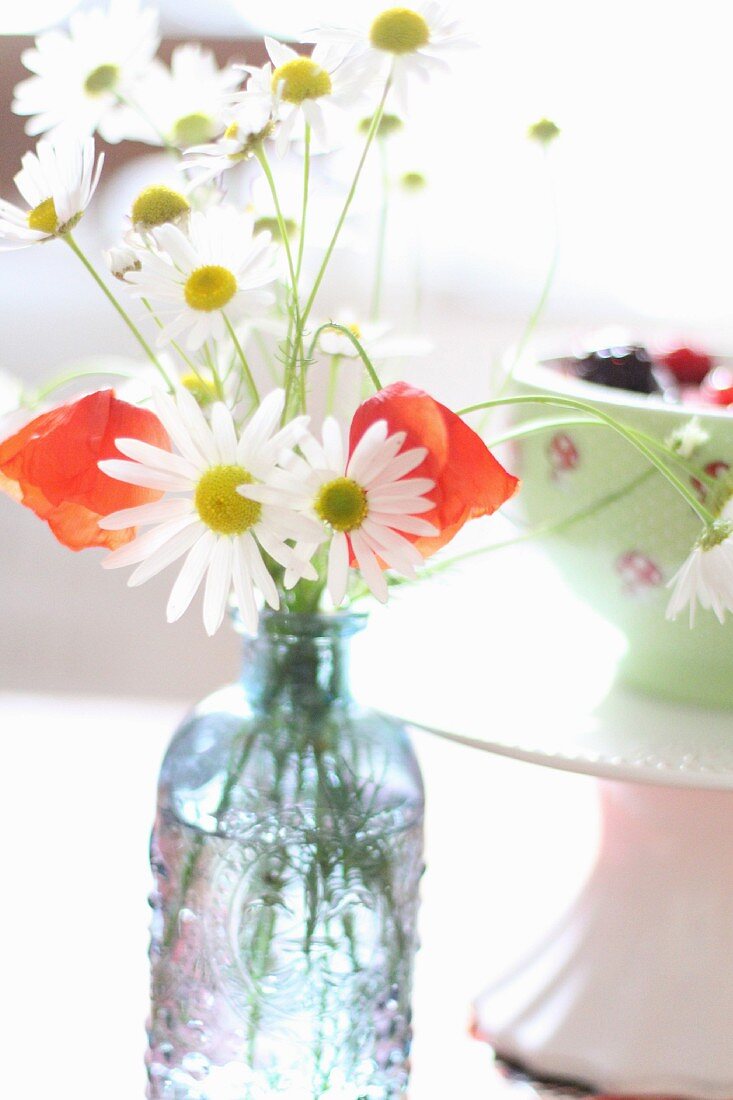Frische Wiesenblumen in Vase vor einem Vanillepudding
