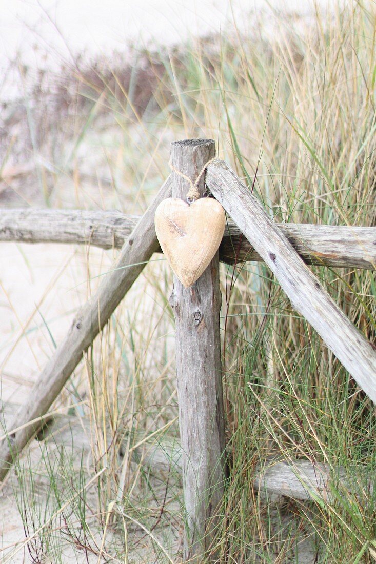 Wooden heart hanging on fence on beach