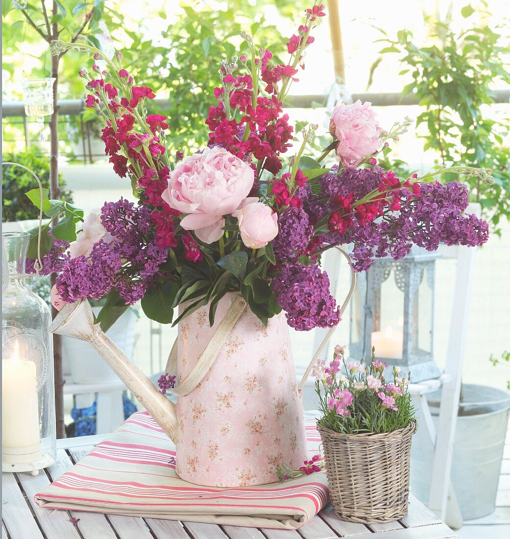 Bouquet of garden flowers with peonies, stocks and lilac in retro watering can with floral pattern