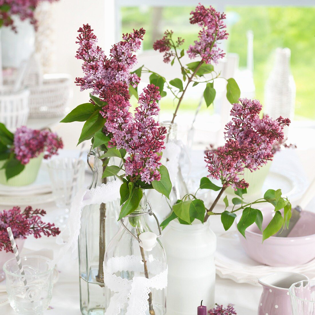 Violette Fliederzweige in verschiedenen Vasen auf gedecktem Tisch