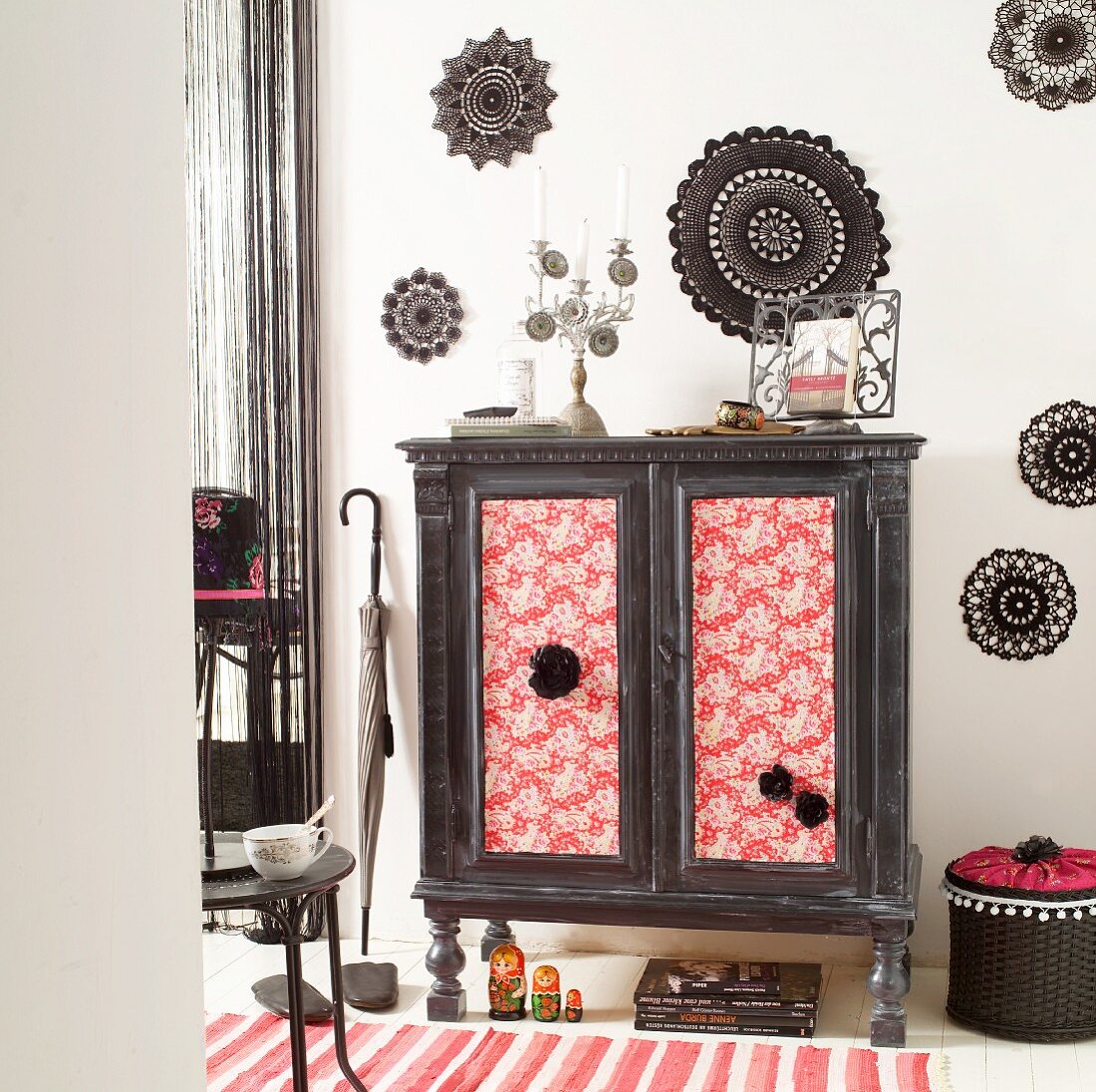 Make-over - vintage cabinet with fabric-covered, ethnic-style doors against wall decorated with black crocheted doilies
