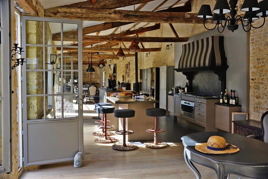 Partially renovated barn - kitchen area with free-standing counter, bar stools and curved vintage table in foreground in open-plan interior