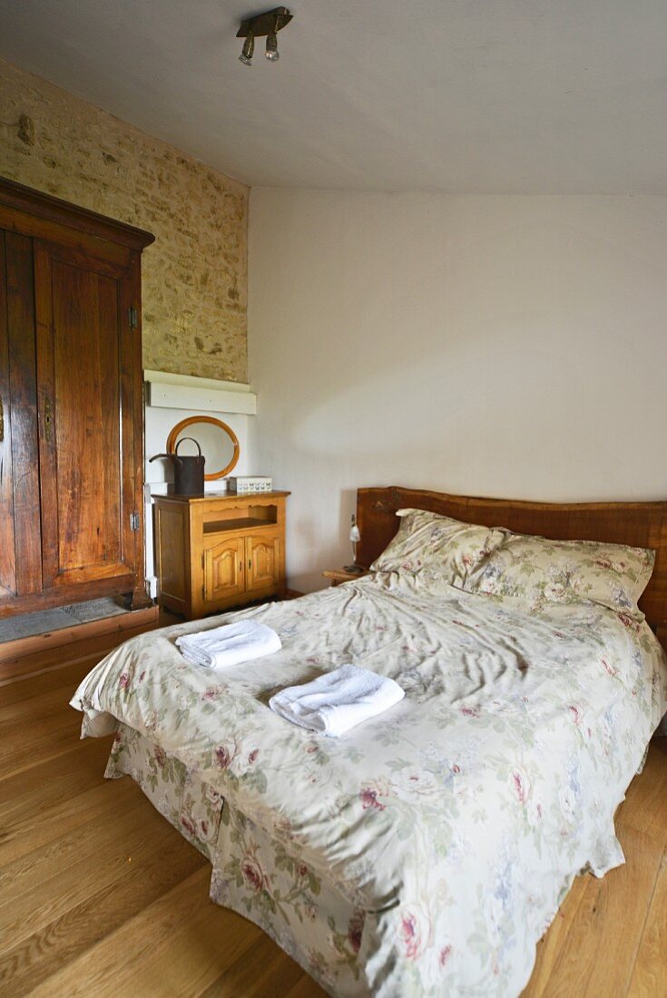 Double bed with delicate floral bed linen and rustic wardrobe in bedroom