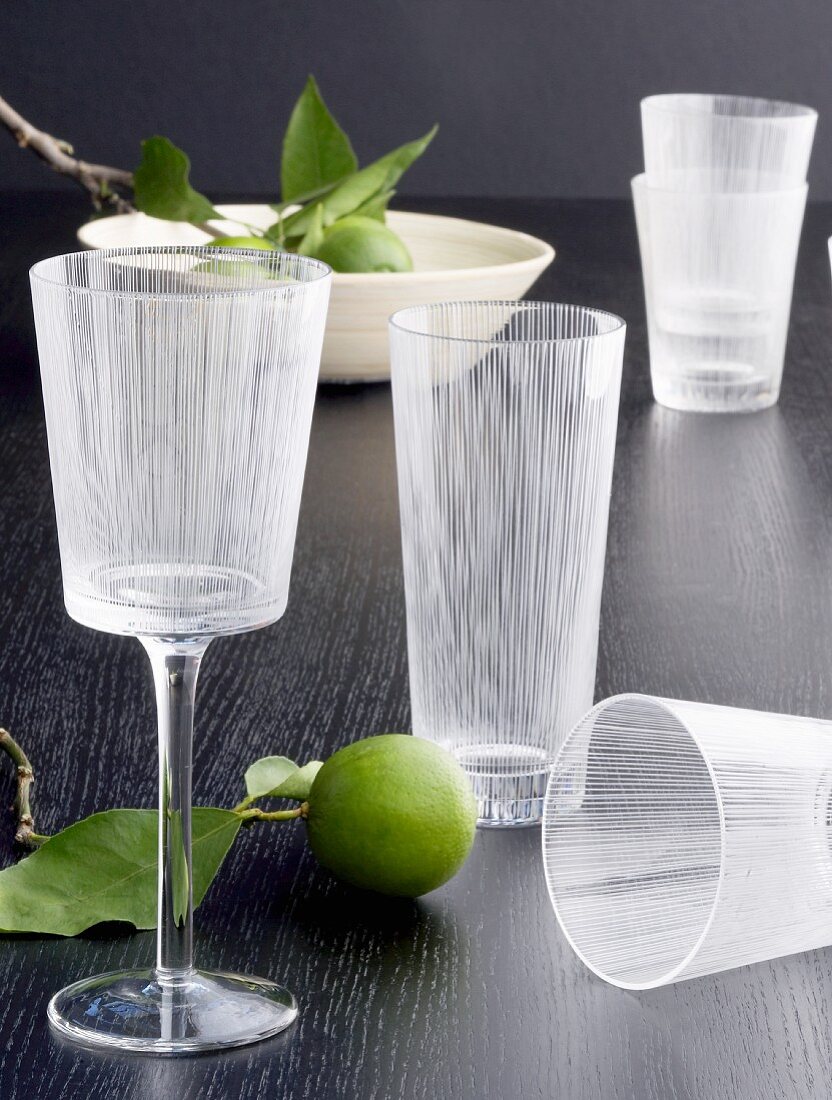 Wein- und Wassergläser mit geätztem Streifendesign und dekorative Limonen auf schwarzer Tischplatte