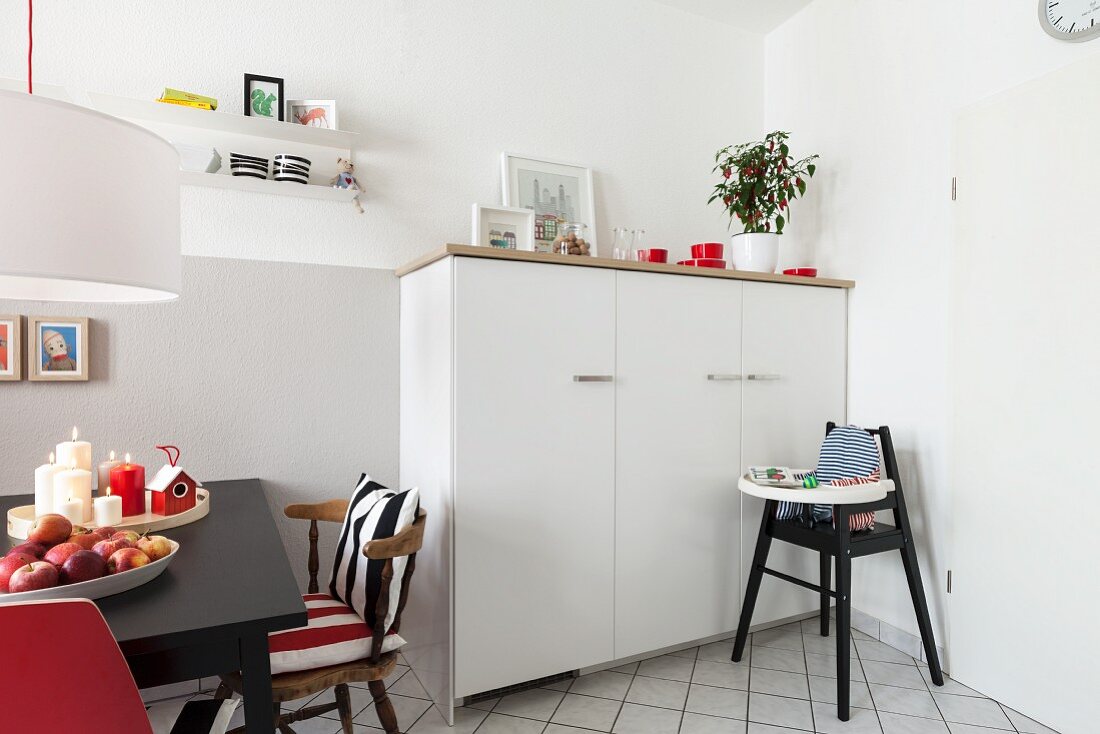 Halbhoher weisser Schrank, davor Kinderhochstuhl, seitlich Essplatz mit schwarzem Tisch in renovierter Wohnküche
