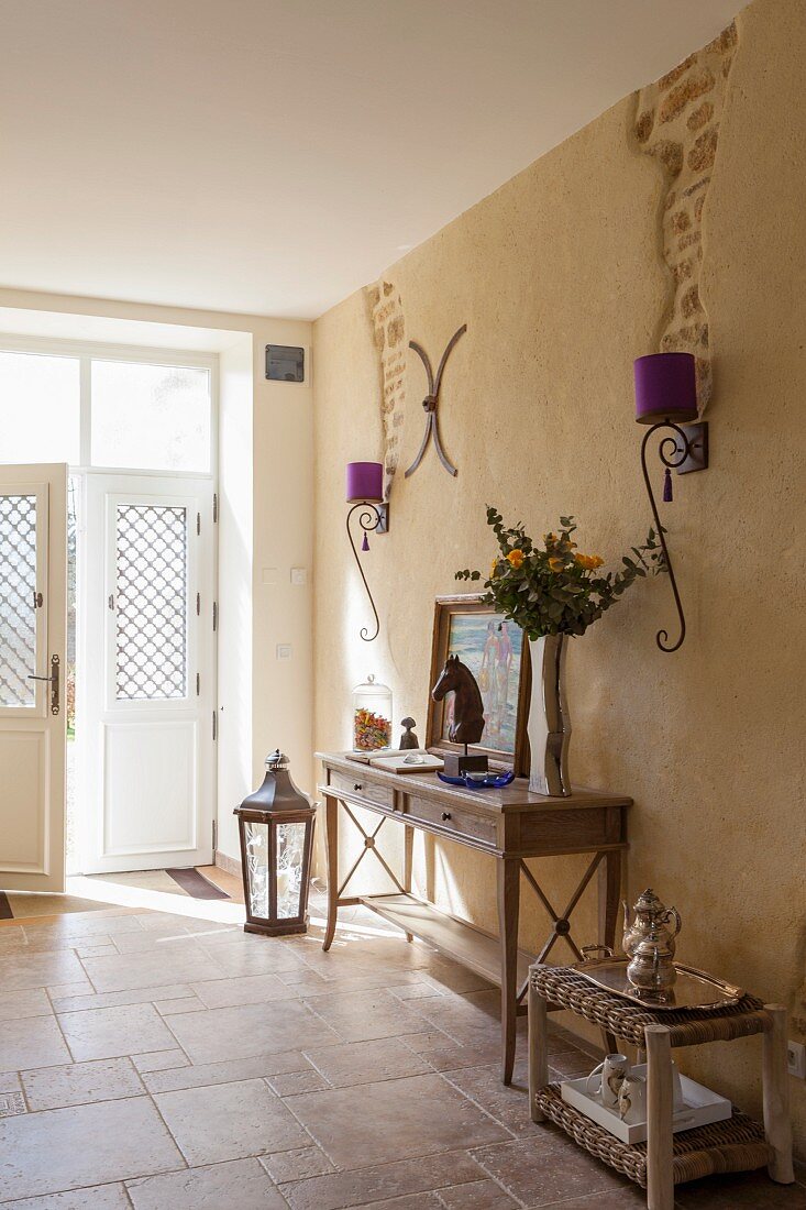 Eleganter traditioneller Hauseingang, Konsolentisch und schmiedeeiserne Wandleuchten mit violettem Lampenschirmen