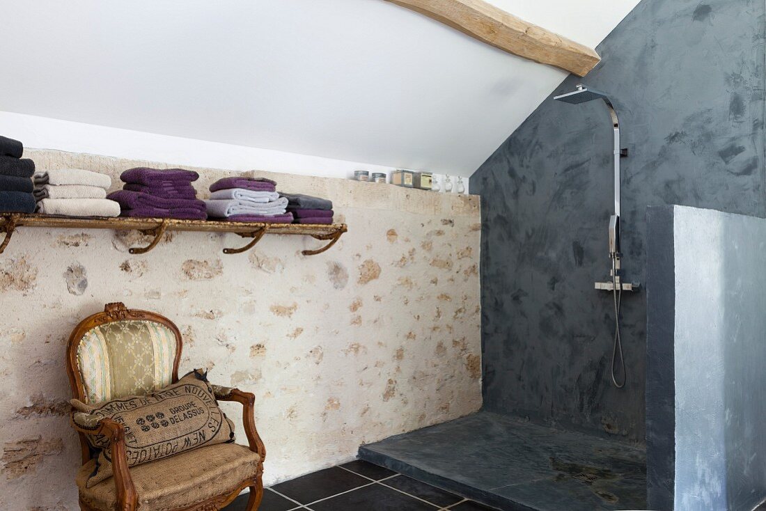 Antique armchair next to slate-grey, modern shower area in renovated country house with stone wall