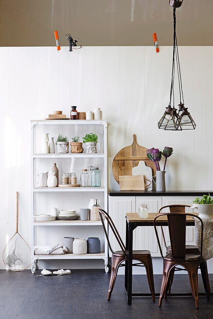 Retro-style metal chairs, dining table and shelves of bottled and storage jars against white-painted wooden wall