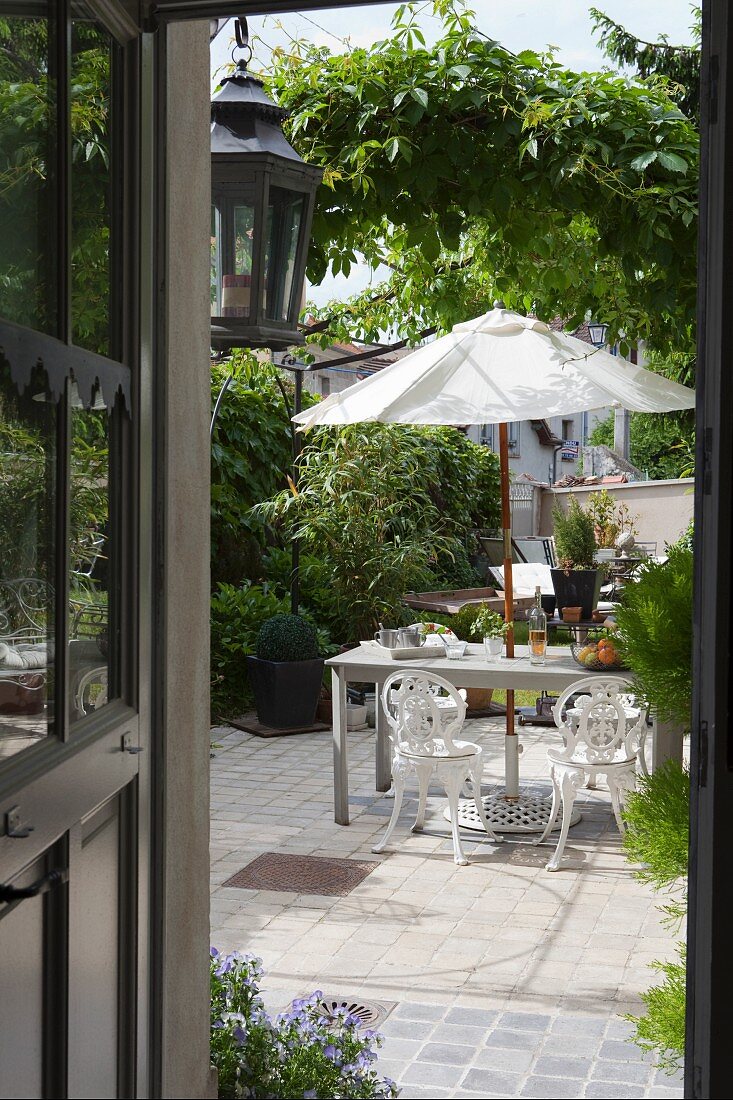 Blick in begrünten idyllischen Innenhof mit nostalgischen Gartenmöbeln unter weißem Sonnenschirm