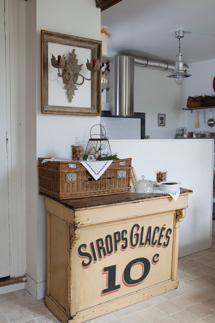 Vintage Schränkchen und Korb vor weisser Brüstungswand, im Hintergrund Edelstahl Dunstabzug in Küche
