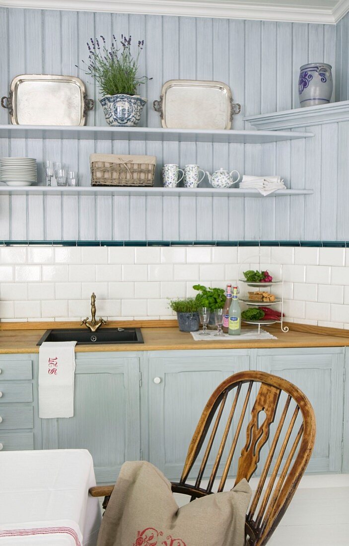 Pastellblaue Landhausküche mit dekorierten Wandborden; Windsor-Stuhl am Esstisch im Vordergrund