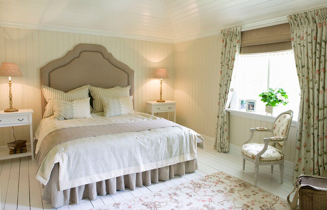 Grand double bed with curved headboard in country-house bedroom with pale wood panelling and fabrics with small floral patterns