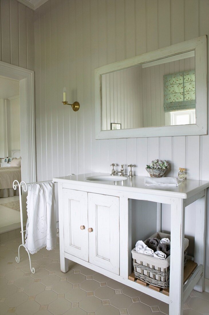 White-painted, wooden washstand cabinet in country-house bathroom with wood-panelled walls painted pale grey