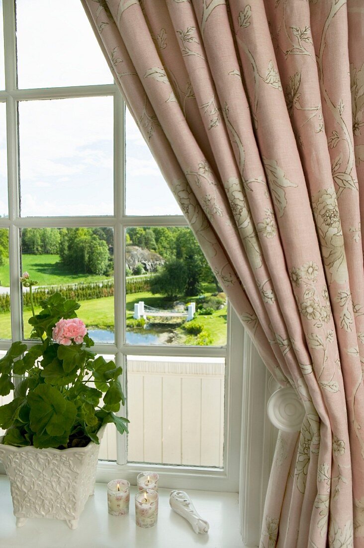Ausblick auf herrschaftlichen Landschaftsgarten durch Fenster mit drapiertem Vorhang und Geranientopf