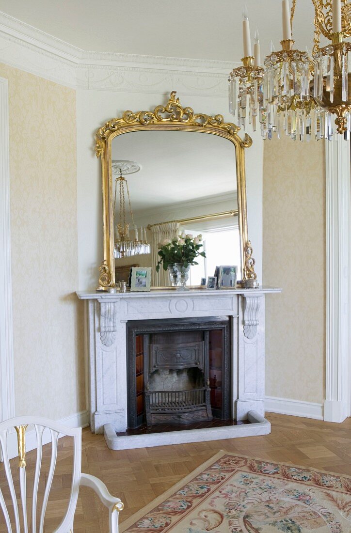 Mirror with magnificent gilt frame above open fireplace in elegant interior with crystal chandelier