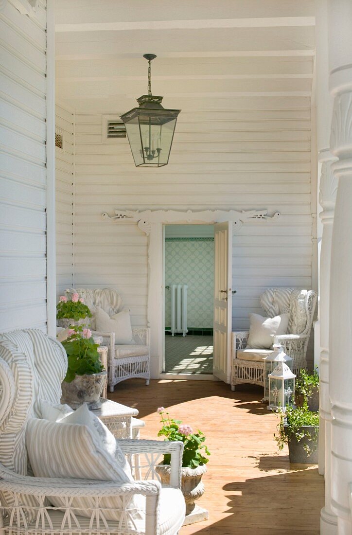 White wicker chairs and geraniums in sunny loggia with white wooden panelling