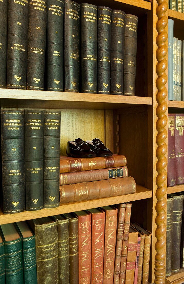 Detail of bookshelves with carved, wooden ornamentation and antiquarian books with gilt-embossed spines