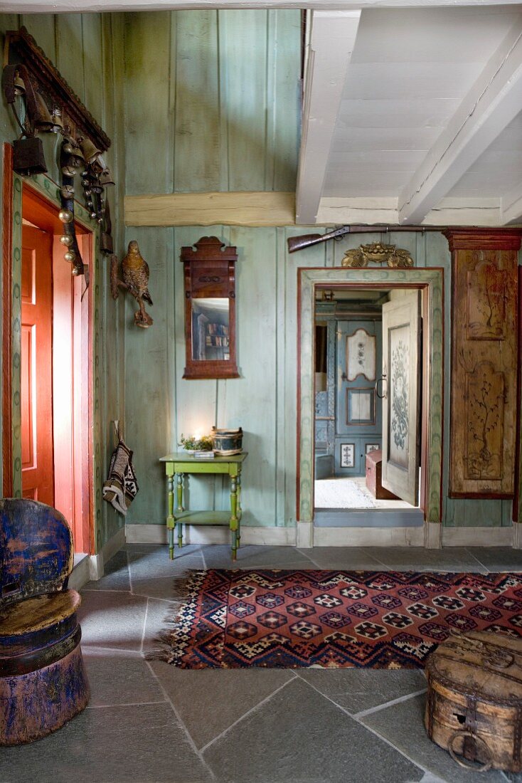 Eingangsbereich eines Holzhauses mit bemalten Wänden, vor offener Zimmertür, Teppichläufer auf Natursteinboden