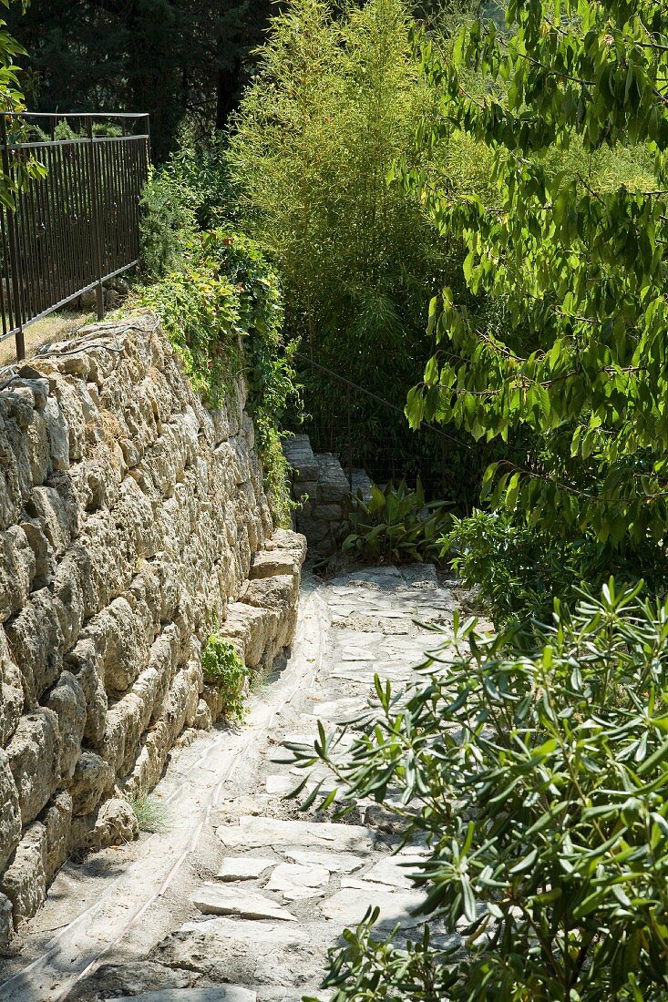 Gepflasterter Weg im Hang mit Abfangung durch seitliche Natursteinmauer in mediterranem Garten
