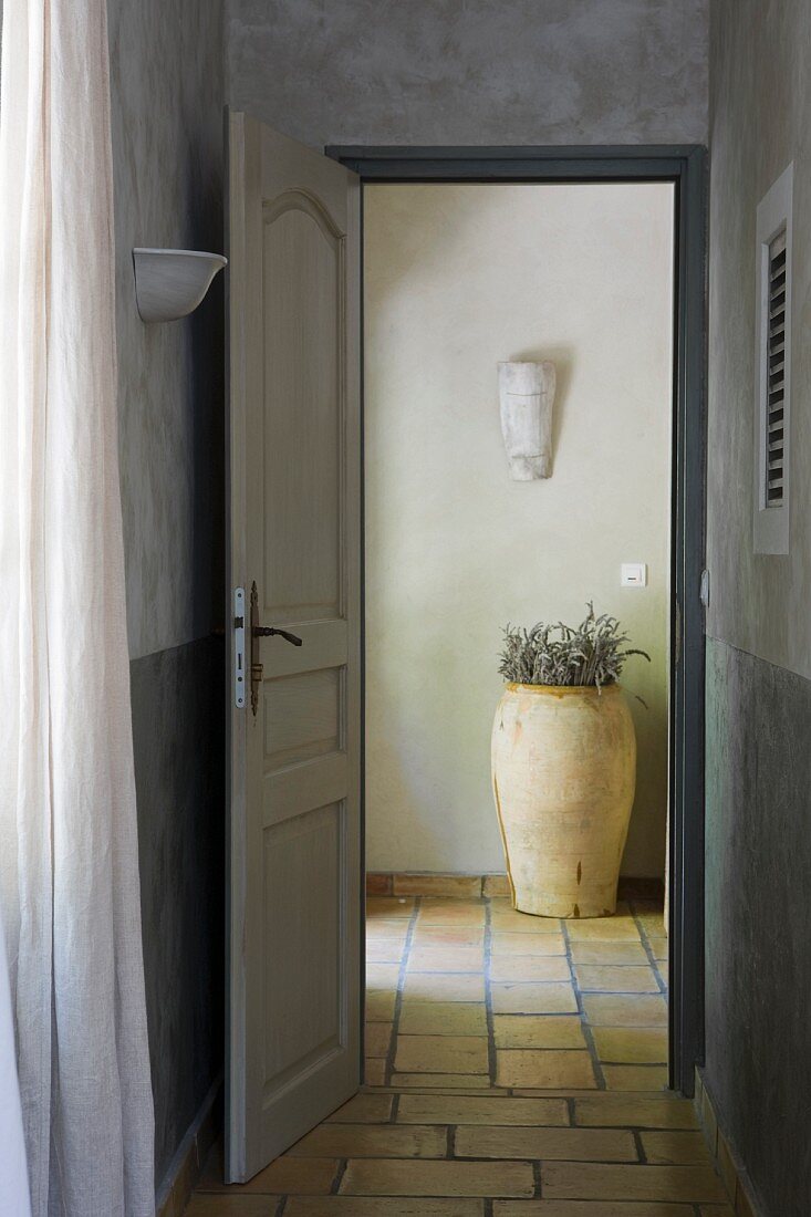Offene Tür zum gefliesten Eingangsbereich mit Terracottatopf
