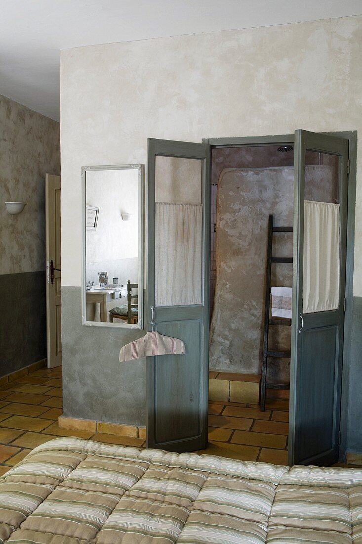 Flügeltür zum Bad Ensuite, in Grautönen marmorierte Wände und gelbliche Terrakottafliesen, vorne Doppelbett mit gestreifter Steppdecke