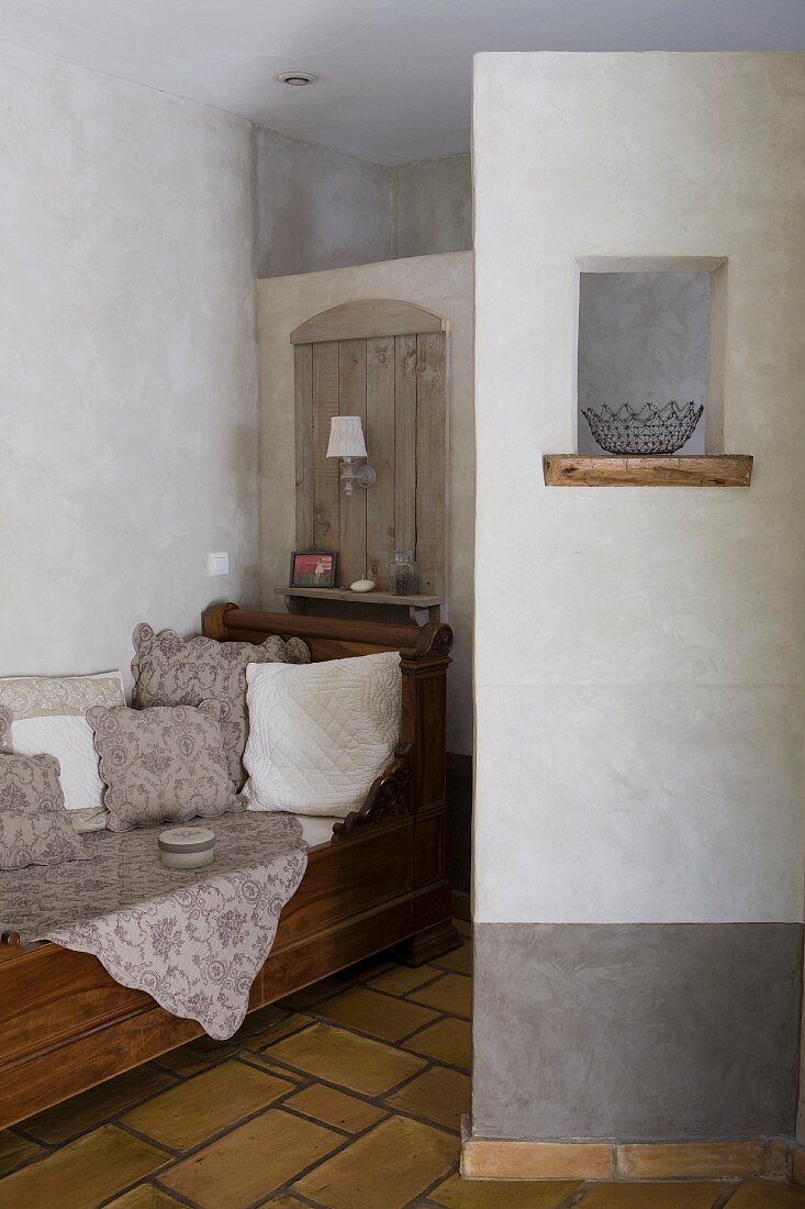 Antike Sofabank mit massiven Seitenteilen vor der Trennwand zur Toilette und Sichtschutzmauer mit dekorativem Fensterchen vor dem Waschtisch