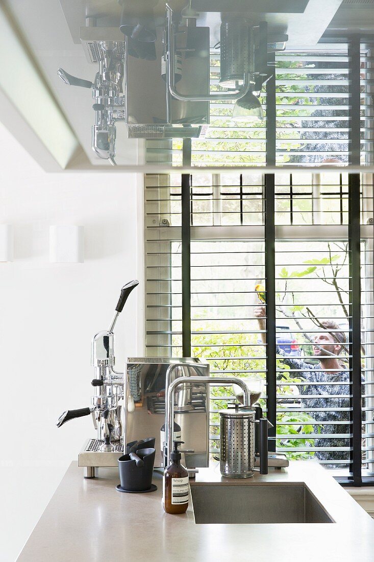Freistehende Kücheninsel mit Spülbecken, Espressomaschine, oberhalb Dunstabzugshaube, im Hintergrund Fenster mit Jalousie