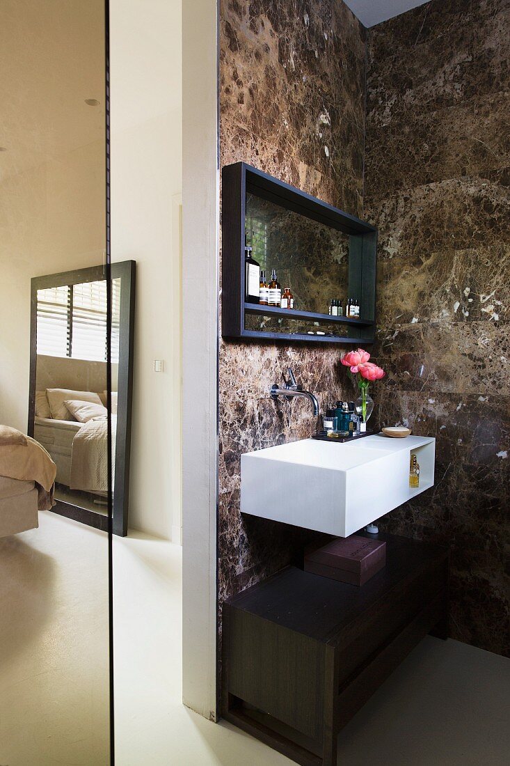 Floating washstand with integrated sink on marble-tiled wall next to doorway leading to bedroom