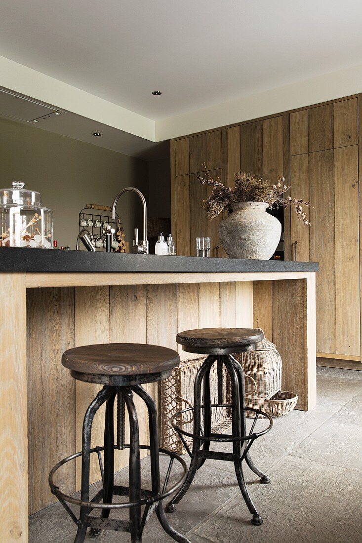 Vintage bar stools at island counter with black worksurface and solid-wood front