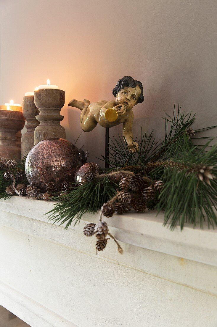 Weihnachtsdeko vor Engelfigur auf Metallstab befestigt und brennende Kerzen auf Holz Kerzenhalter auf Ablage