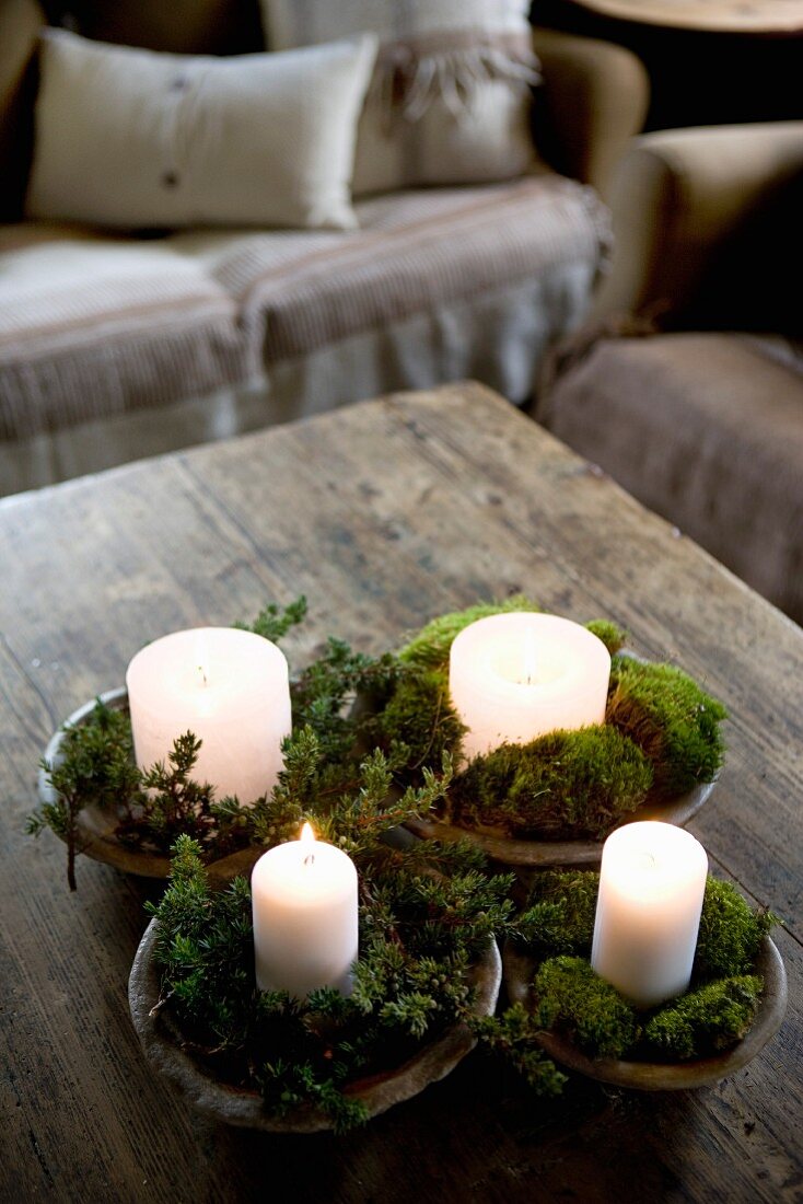 Moos und kleine Zweige um brennende Kerzen dekoriert, in Holzschalen