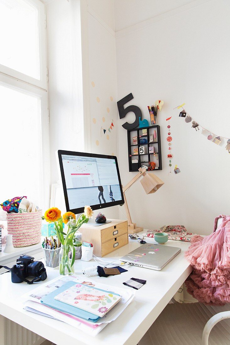 Blumenstrauss neben Monitor und Laptop auf weißem Schreibtisch
