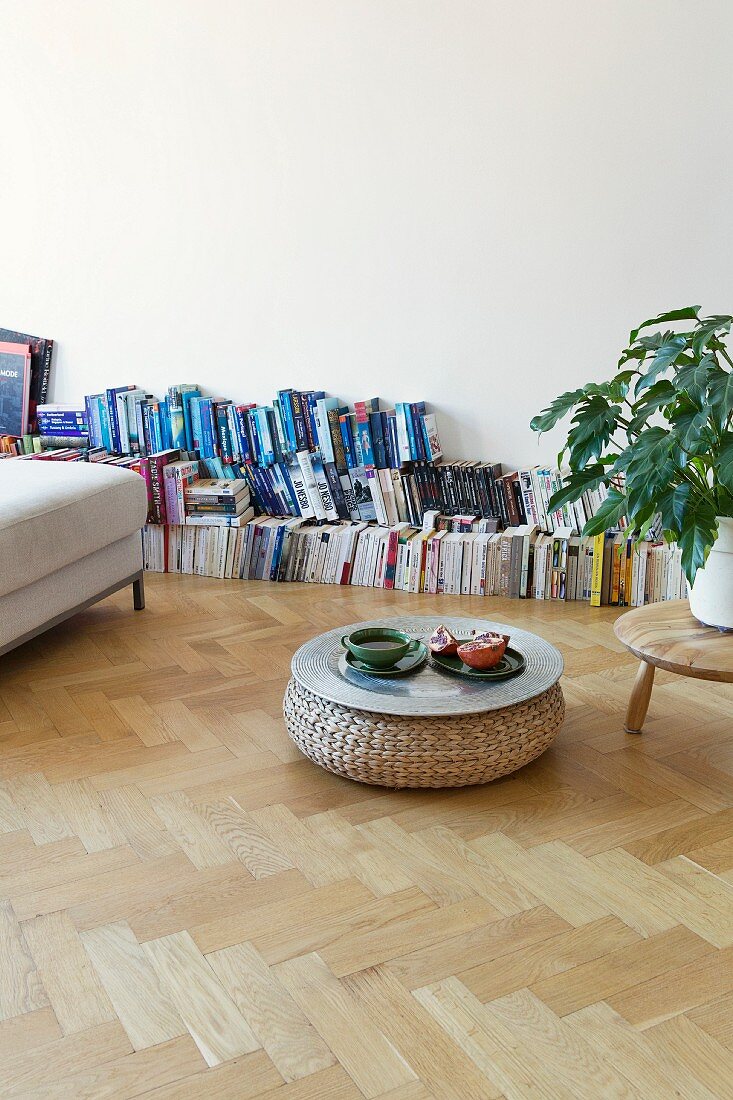 Books lined up against wall and tray of pouffe used as coffee table in spacious room in period apartment