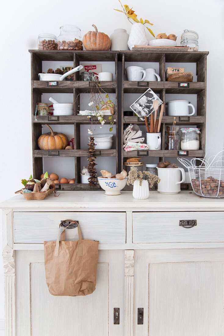 White-painted dresser with crockery and autumnal decorations in old display cases on top