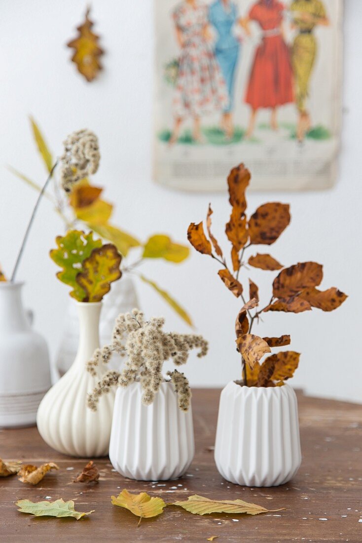 weiße Keramikvasen mit herbstlichen Blätterzweigen auf Tisch