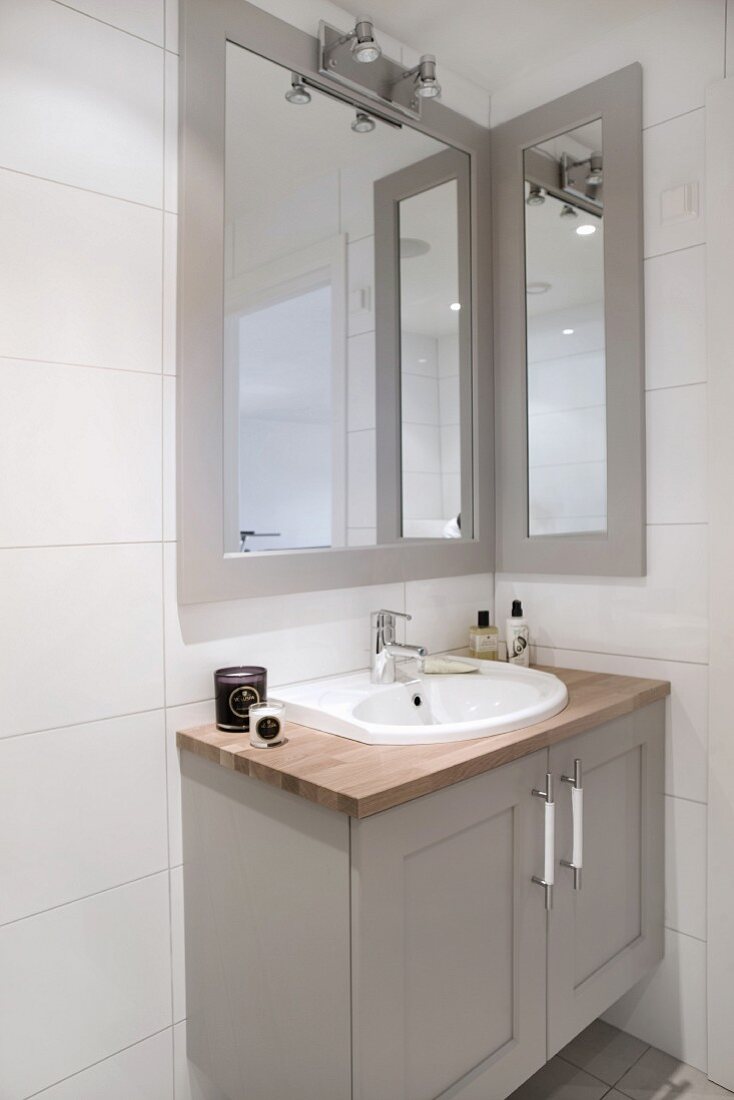 Waschtisch mit grau lackiertem Unterschrank und gerahmter Spiegel oberhalb Wandleuchte in Badezimmerecke